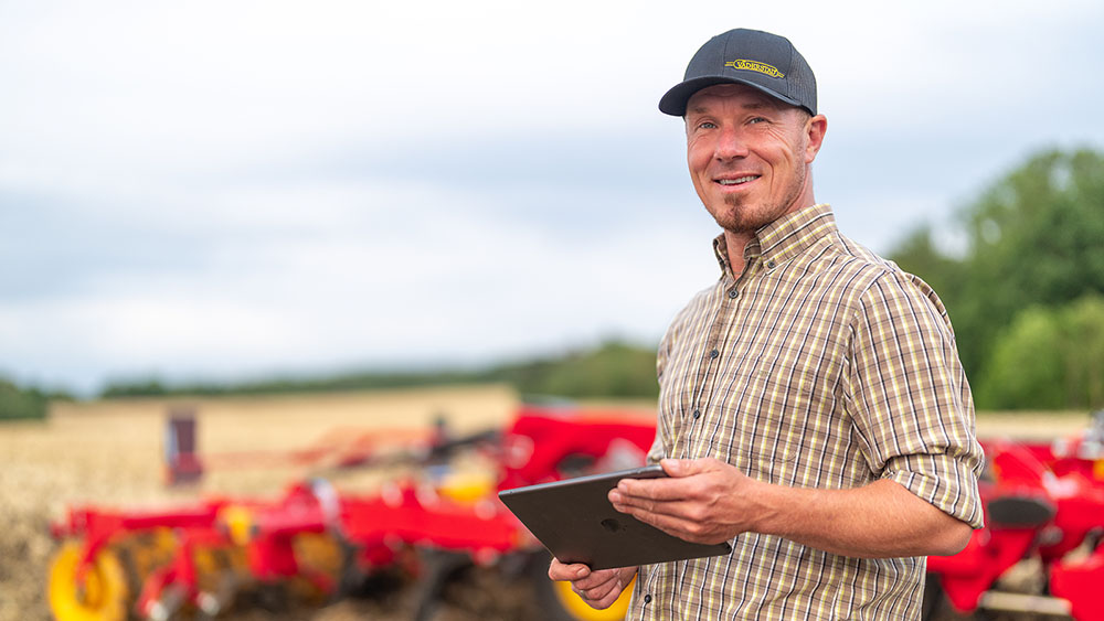 Un hombre sonriente delante de un TopDown con una gorra Väderstad 